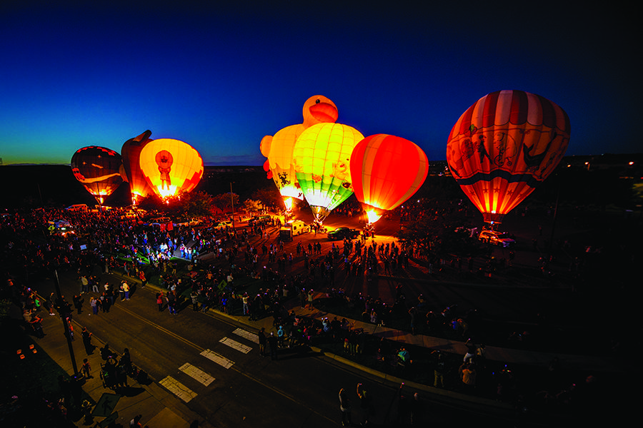 Multiple hot air balloon floating in the SJC parking lot with a large crowd around